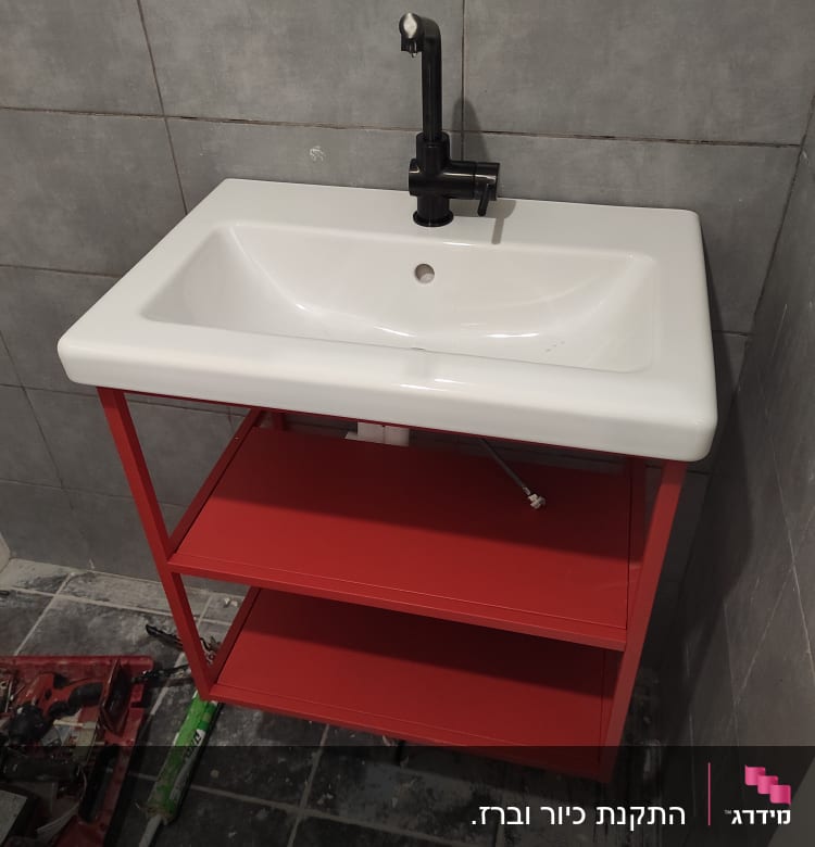 כיור עם ברז שחור ומדף אדום, כלים על הרצפה
